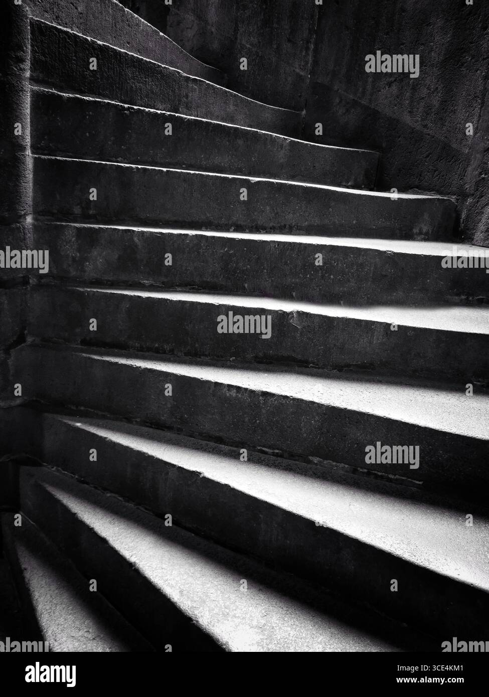 Eine Wendeltreppe aus Stein führt nach oben. Die glatten, strukturierten Stufen werden durch dunkles Licht hervorgehoben - Smartphone-aufgenommenes Stockfoto