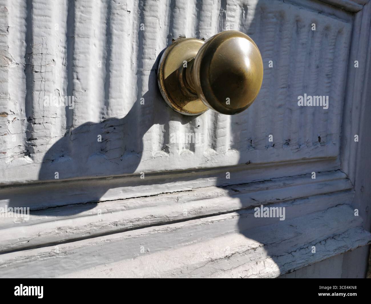 Nahaufnahme eines alten Messingknaufs, der an einer verwitterten weißen Holztür befestigt ist. Frankreich Stockfoto