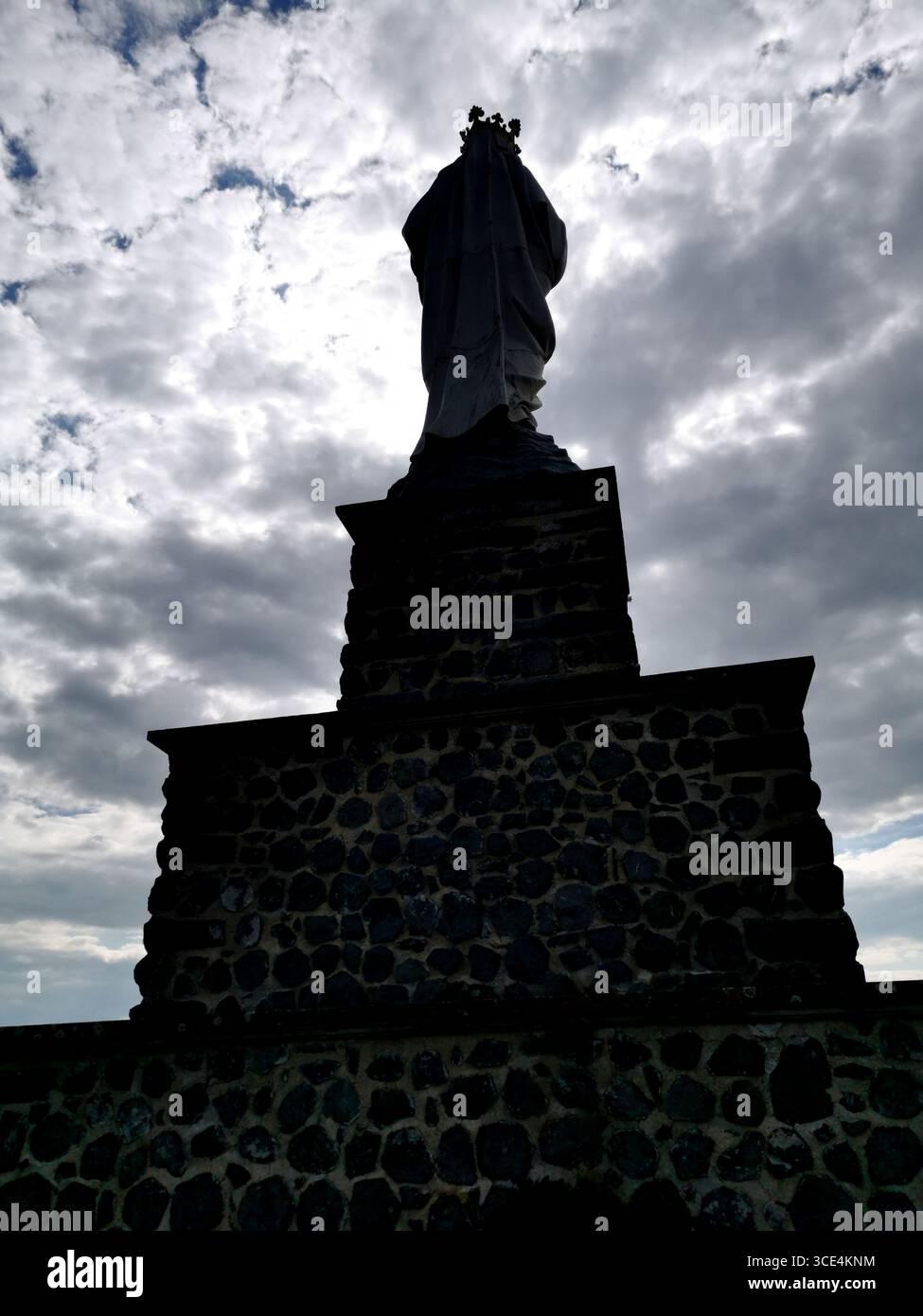 Eine große, unberührte Statue steht auf einem Steinsockel, die sich vor einem dramatisch bewölkten Himmel befindet. Auvergne. Frankreich - Smartphone-aufgenommenes Stockfoto