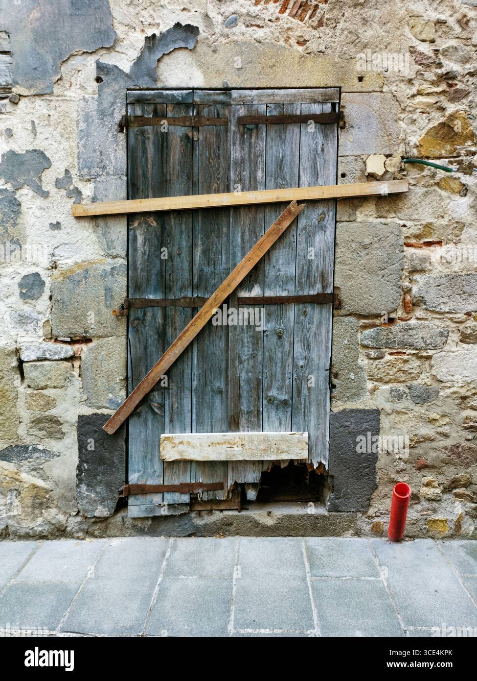Eine rustikale Holztür ist mit einem abgewinkelten Balken gegen eine strukturierte Steinmauer in einer engen alten Straße gesichert. Frankreich - Smartphone-aufgenommenes Stockfoto