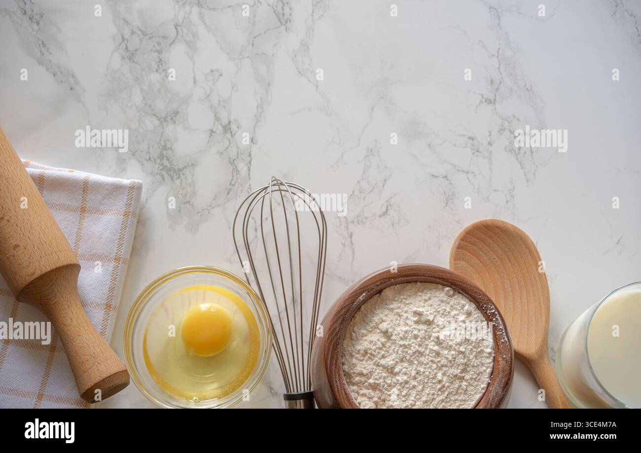 Zutaten und Werkzeuge sind ordentlich angeordnet, einschließlich Mehl, ein Ei und Backutensilien, was die Zubereitung eines Rezepts in der Küche andeutet. Stockfoto