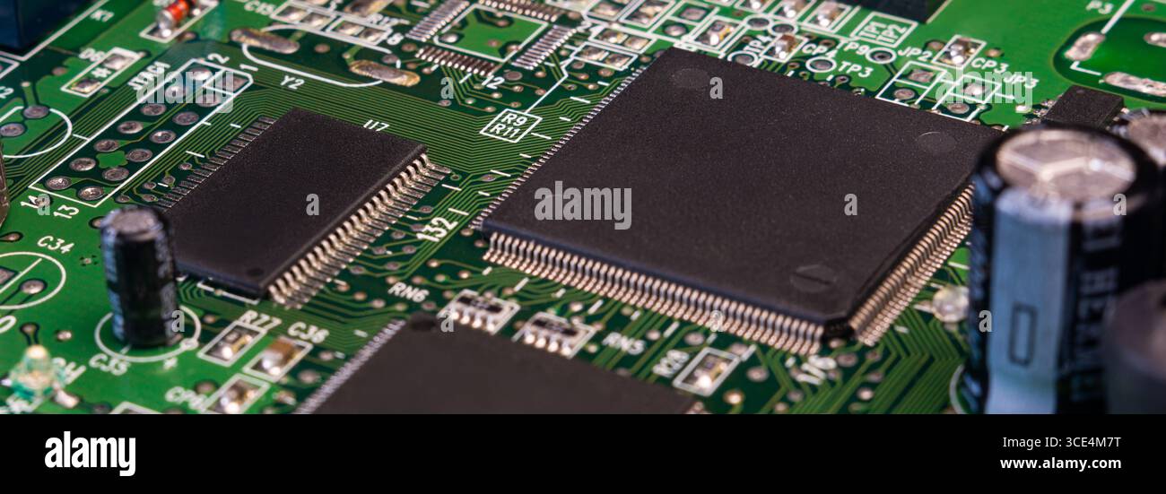 Detaillierter Blick auf eine Leiterplatte mit integrierten Schaltungen, Kondensatoren und kompliziertem Löten auf einer grünen Oberfläche. Stockfoto