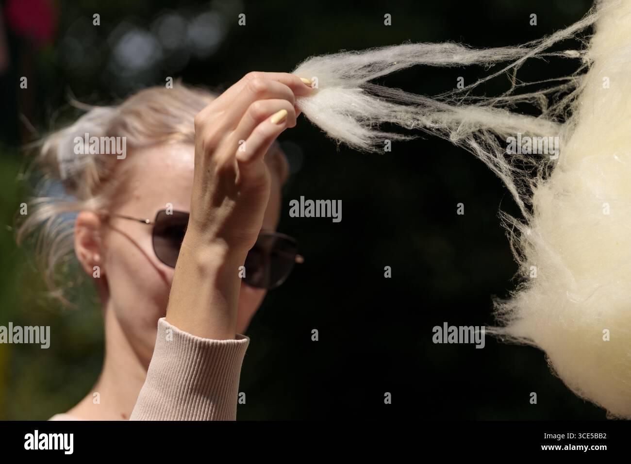 Das Bild zeigt eine Frau, die ein flauschiges Stück Zuckerwatte hält und einen verspielten Moment genießt. Sie trägt eine Sonnenbrille und verkörpert den unbeschwerten Geist von s Stockfoto
