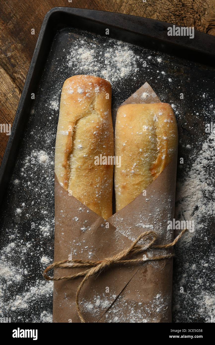 Zwei frisch gebackene Baguettes auf einem Backblech, in braunes Papier gewickelt, mit Garn gebunden, mit Mehl bestreut. Stockfoto