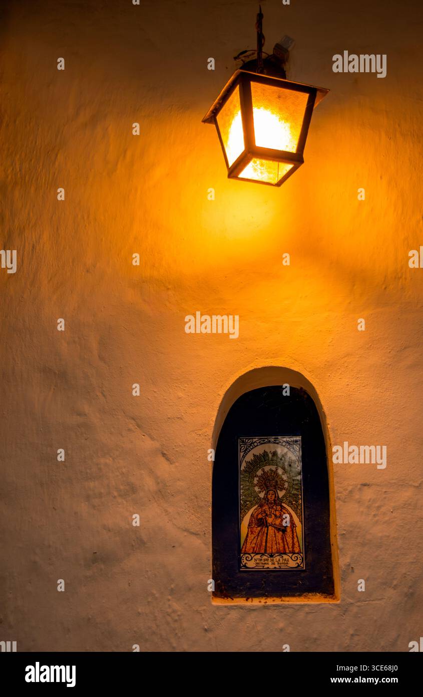 Eine bezaubernde Wandlaterne, die eine Nische mit einem lebendigen religiösen Bild in Villa de Leyva, Boyaca, Kolumbien, beleuchtet. Stockfoto