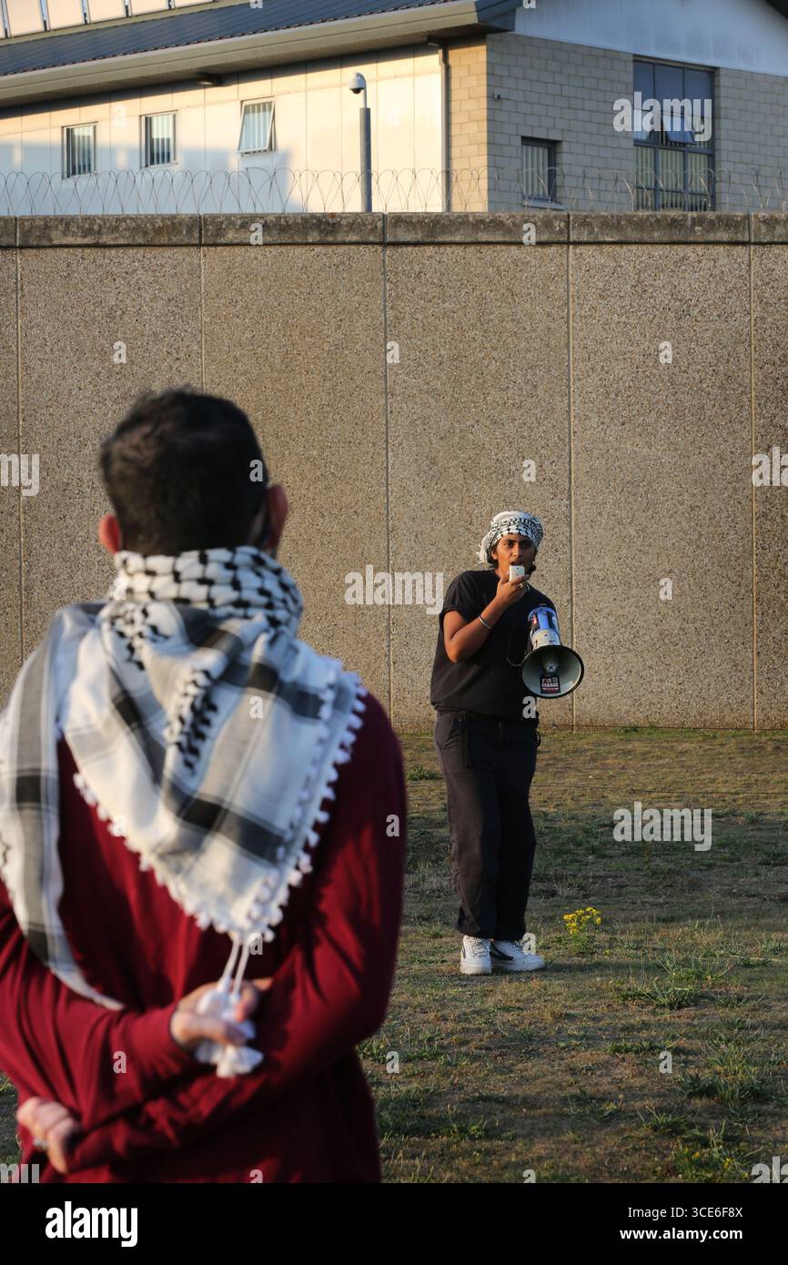 Ein Demonstrant spricht durch ein Megaphon während eines Prisoners4Palestine Starts bei einer Kundgebung vor HMP Peterborough. Prisoners4Palestine ist eine kollektive Anstrengung, um sich denjenigen innerhalb des Gefängnissystems anzuschließen, die Maßnahmen gegen Völkermord, Imperialismus und Unterdrückung ergriffen haben und jetzt dafür brutal bestraft werden. Das Gefängnis beherbergt drei der Filton24-Gefangenen, einer befindet sich derzeit im Hungerstreik. Die Kundgebung ist ein Jahr her, seit die Filton-Gefangenen in Untersuchungshaft genommen wurden und ehrt den Hungerstreik der palästinensischen Gefangenen von 2004. Sie verlangen, dass Elbit Systems heruntergefahren wird, freie Assoziation Stockfoto