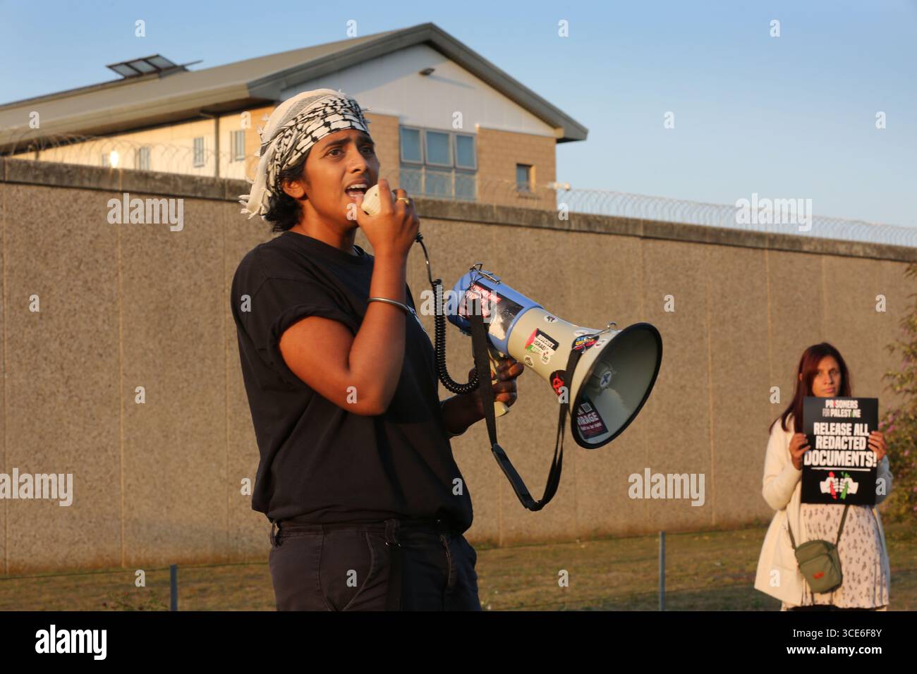 Ein Demonstrant spricht durch ein Megaphon während eines Prisoners4Palestine Starts bei einer Kundgebung vor HMP Peterborough. Prisoners4Palestine ist eine kollektive Anstrengung, um sich denjenigen innerhalb des Gefängnissystems anzuschließen, die Maßnahmen gegen Völkermord, Imperialismus und Unterdrückung ergriffen haben und jetzt dafür brutal bestraft werden. Das Gefängnis beherbergt drei der Filton24-Gefangenen, einer befindet sich derzeit im Hungerstreik. Die Kundgebung ist ein Jahr her, seit die Filton-Gefangenen in Untersuchungshaft genommen wurden und ehrt den Hungerstreik der palästinensischen Gefangenen von 2004. Sie verlangen, dass Elbit Systems heruntergefahren wird, freie Assoziation Stockfoto