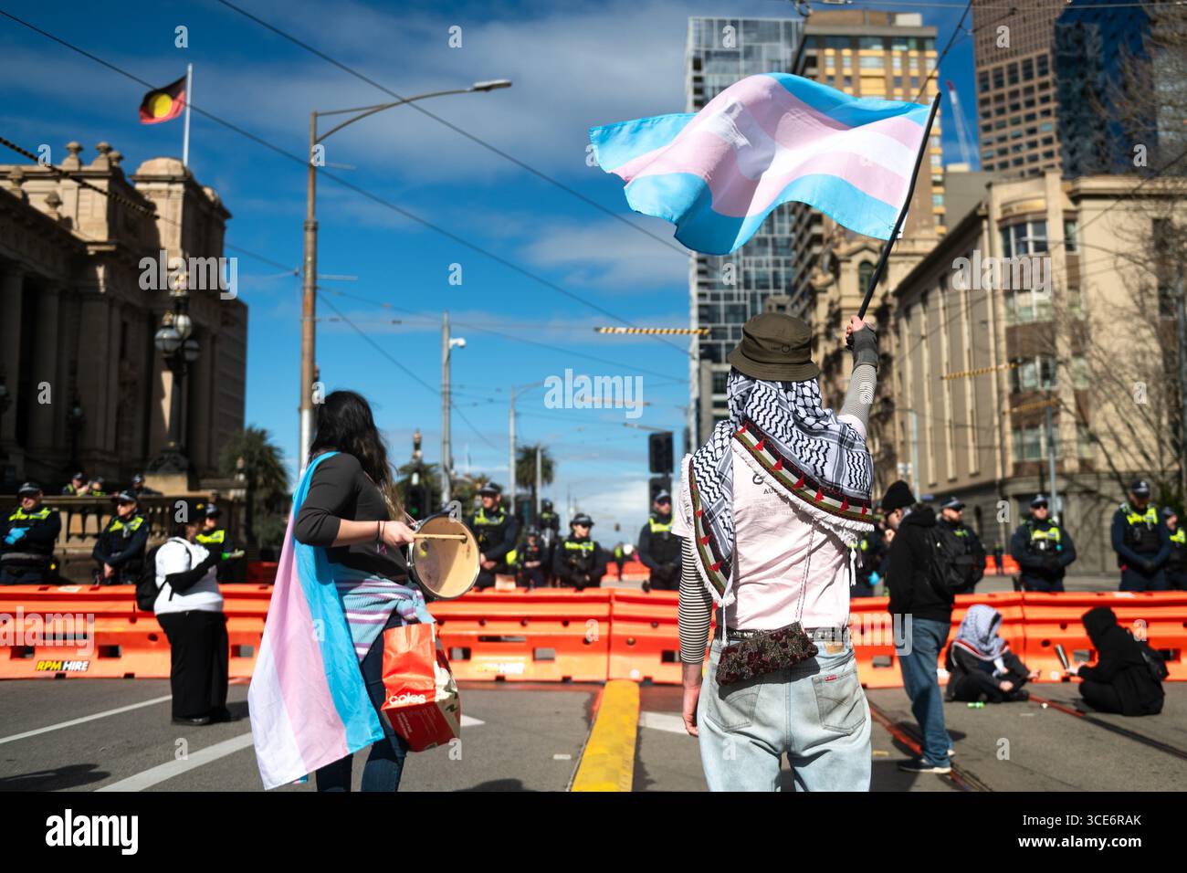 August 2025, Melbourne, Australien. Ein Transgender-Rechteaktivist schwenkt die Transgender-Flagge, während ein anderer während eines Gegenprotests gegen eine Anti-Trans-Kundgebung mit dem Schlagzeug spielt. Quelle: Jay Kogler/Alamy Live News Stockfoto