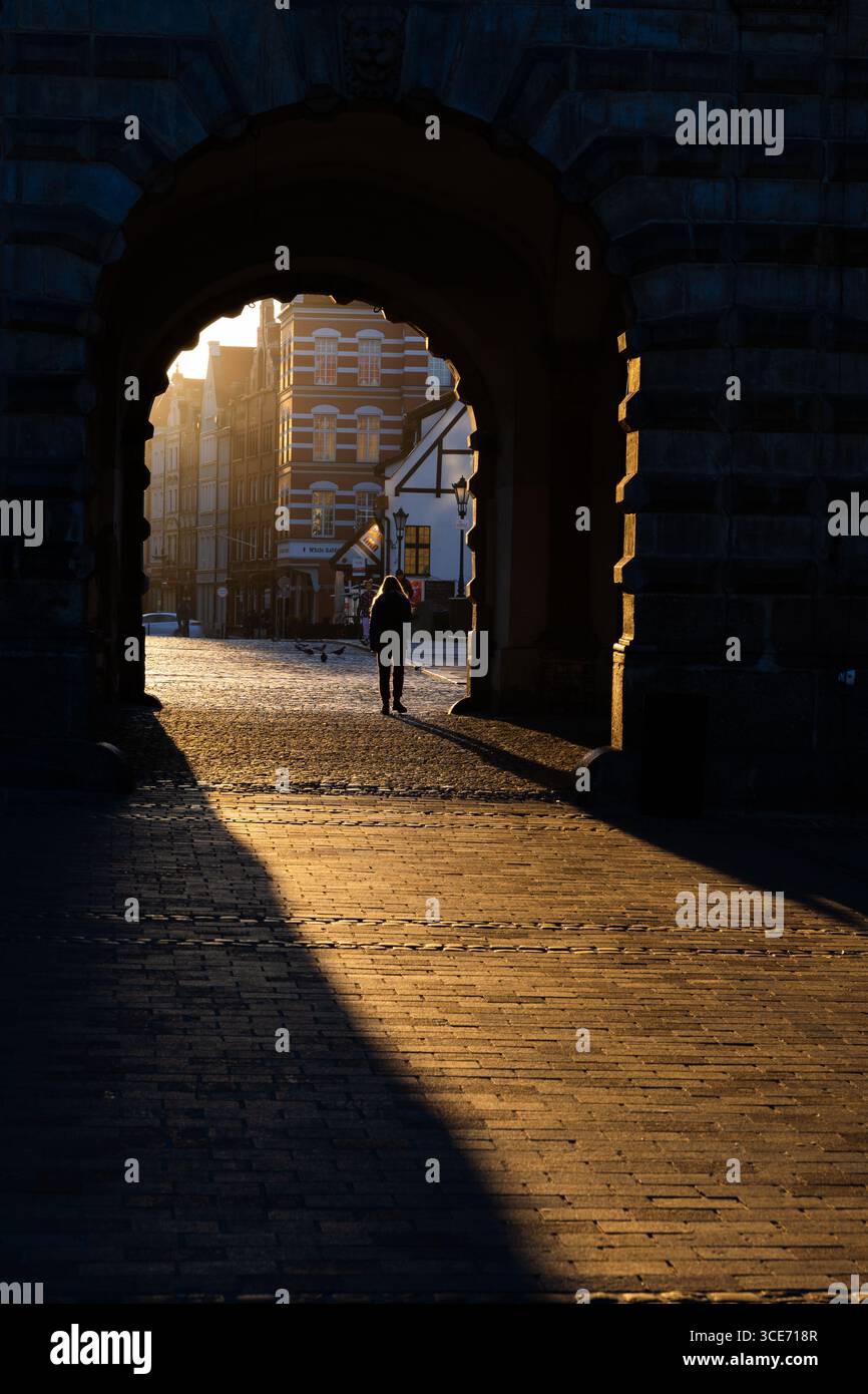 Person im Morgensonnenlicht, das bei Sonnenaufgang durch das Grüne Tor in der Altstadt von Danzig in Polen leuchtet. Stockfoto
