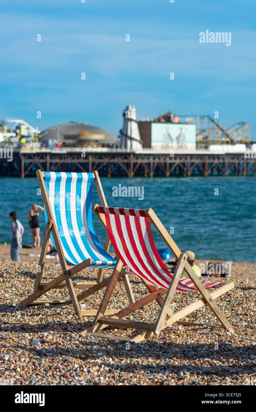 Blaue und rote Liegestühle mit Brighton Palace Pier im Hintergrund Stockfoto
