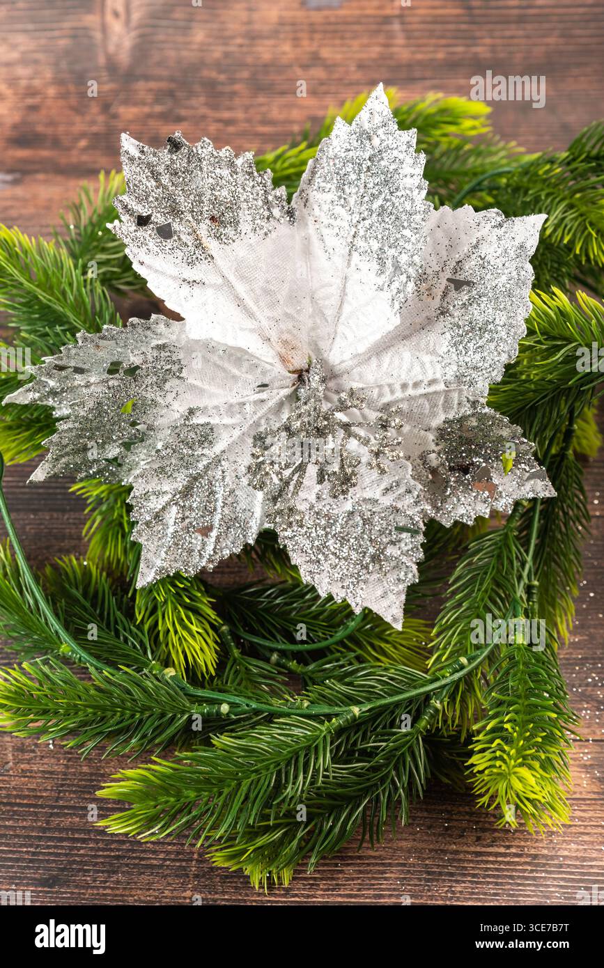 Funkelnde silberne Weihnachtsstern auf Kieferkranz über rustikalem Holz. Elegante handgefertigte Dekoration für Weihnachtsbasteln, Heimwerkerprojekte und Winterferien Stockfoto