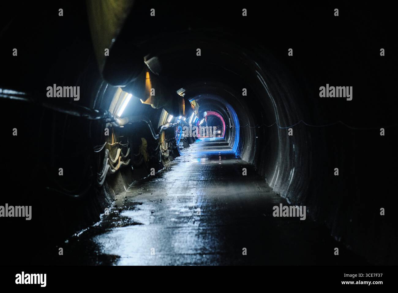 Beleuchteter Wasserkrafttunnel mit nassem Betonboden Stockfoto