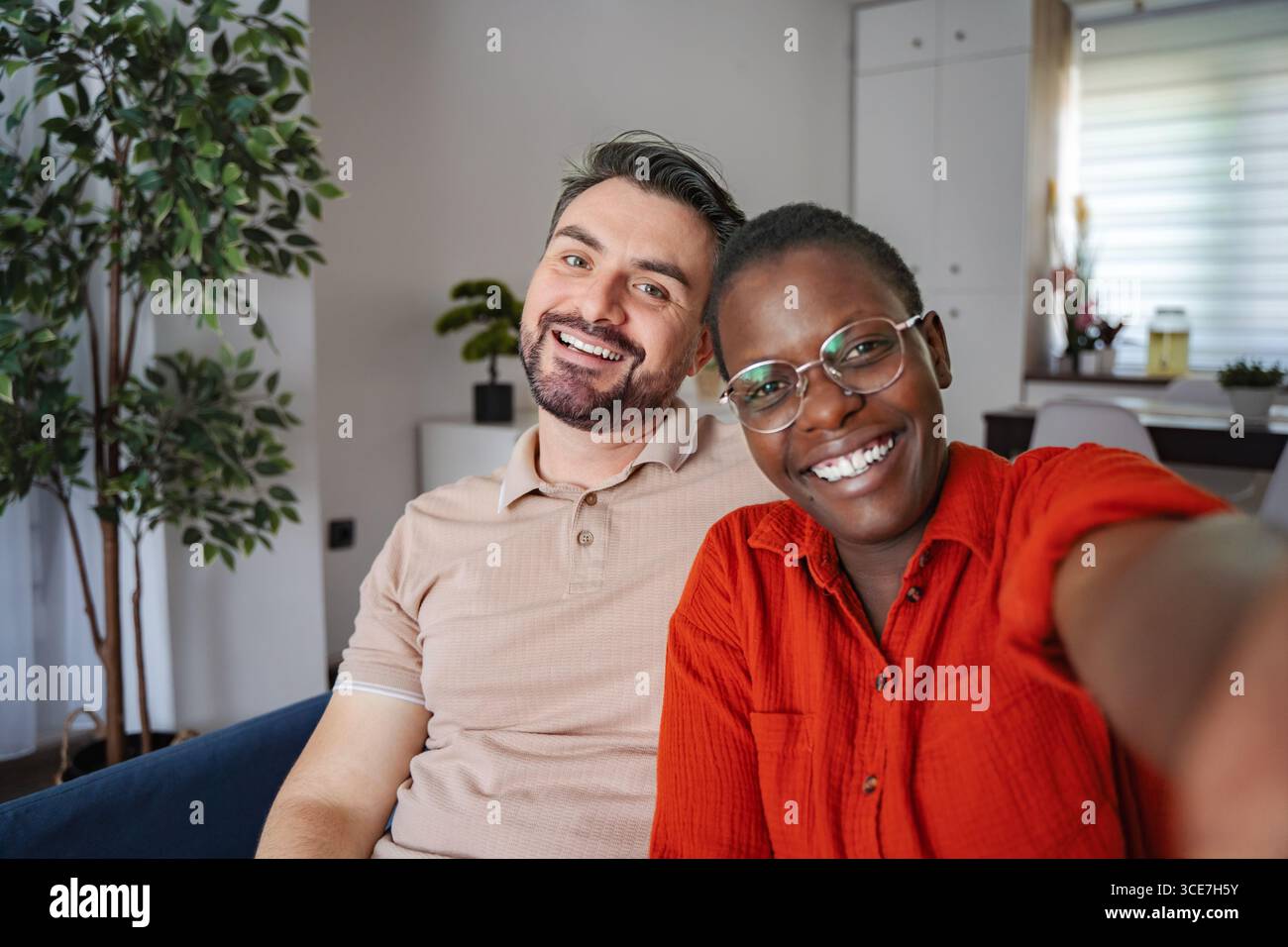Glückliches Multi-ethnisches Paar, das zu Hause ein Selfie auf der Couch macht Stockfoto