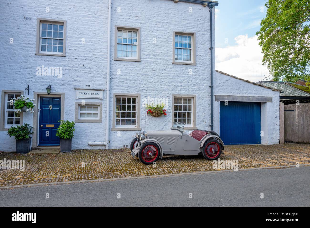 Vollständig restaurierte MG J2 Midget in Hellgrau gestrichen und auf einem Kopfsteinpflaster vor einem weiß gemalten Steinhaus stehend. Stockfoto
