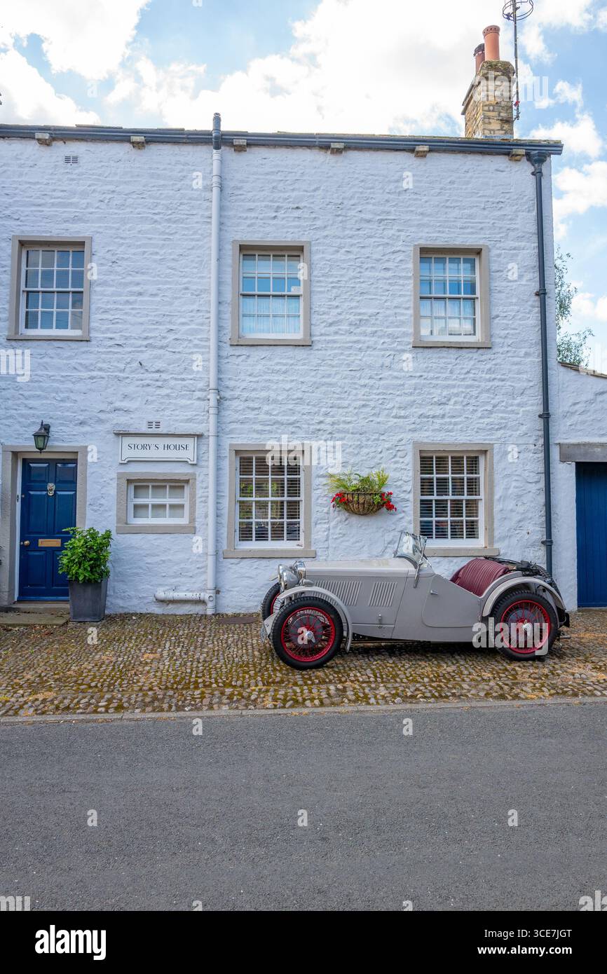 Vollständig restaurierte MG J2 Midget in Hellgrau gestrichen und auf einem Kopfsteinpflaster vor einem weiß gemalten Steinhaus stehend. Stockfoto