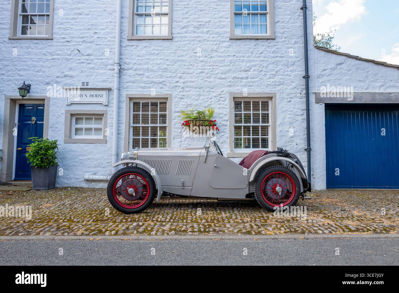 Vollständig restaurierte MG J2 Midget in Hellgrau gestrichen und auf einem Kopfsteinpflaster vor einem weiß gemalten Steinhaus stehend. Stockfoto
