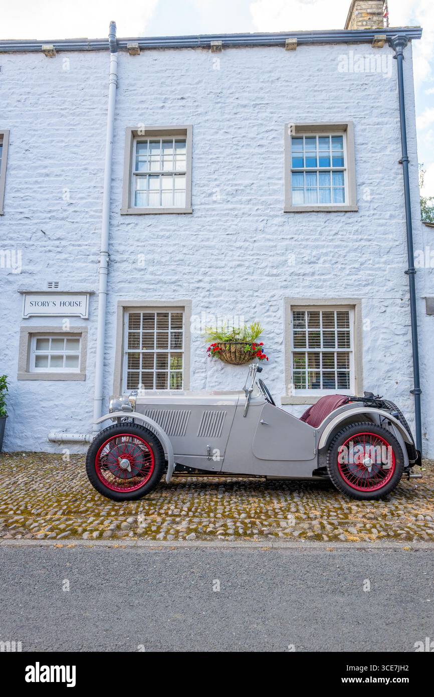 Vollständig restaurierte MG J2 Midget in Hellgrau gestrichen und auf einem Kopfsteinpflaster vor einem weiß gemalten Steinhaus stehend. Stockfoto