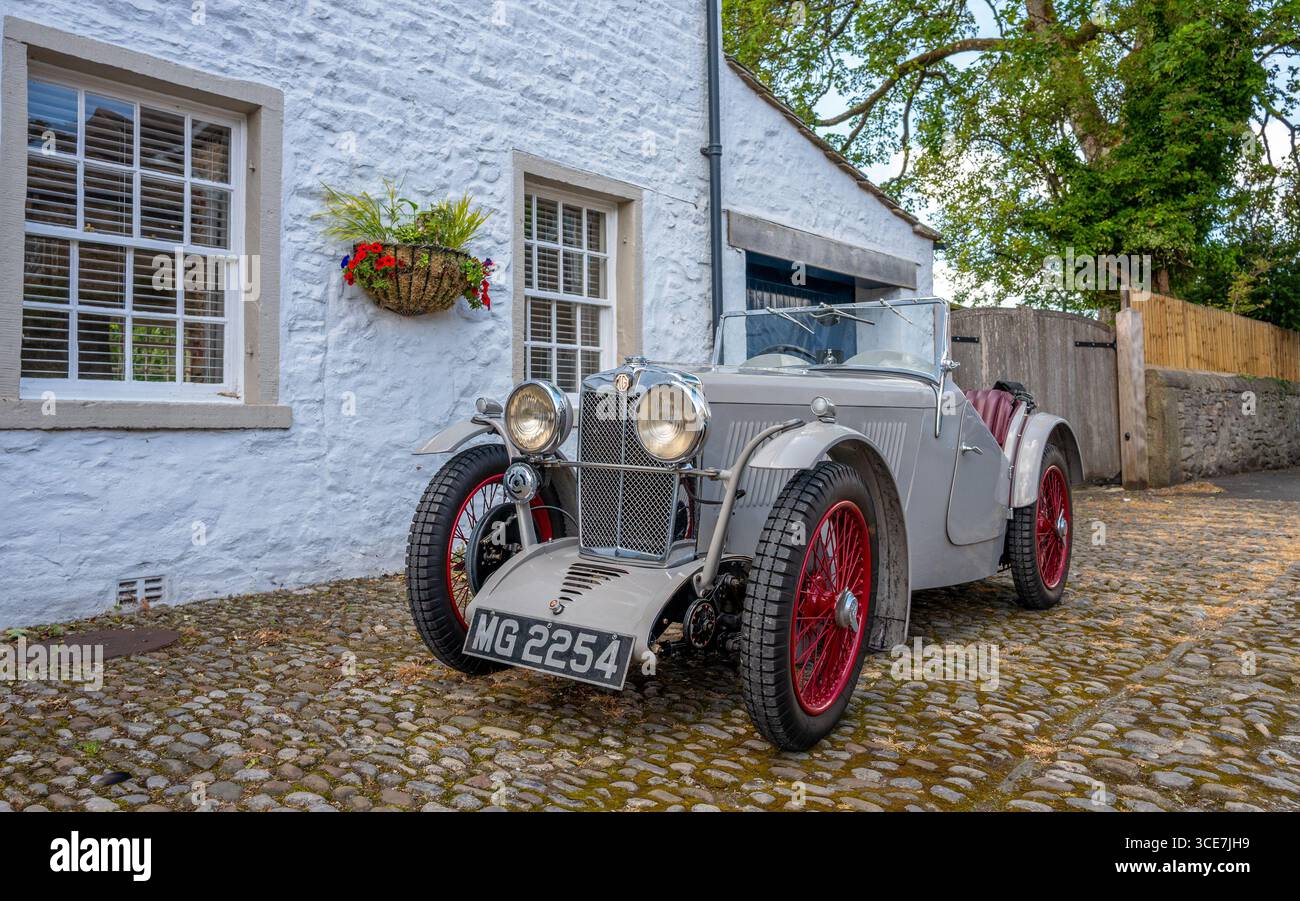 Vollständig restaurierte MG J2 Midget in Hellgrau gestrichen und auf einem Kopfsteinpflaster vor einem weiß gemalten Steinhaus stehend. Stockfoto