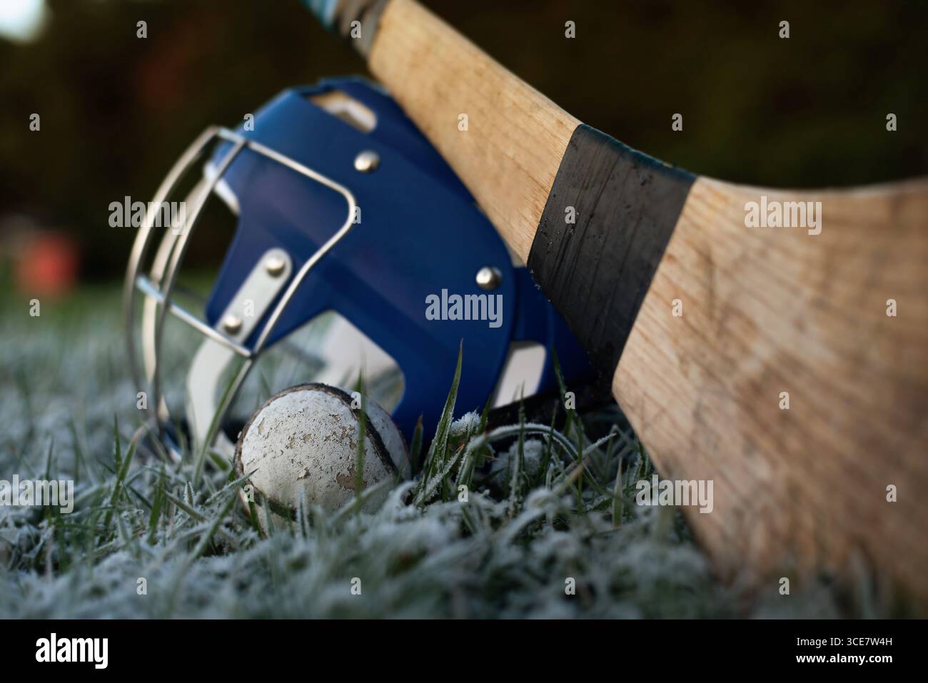 Schleuderausrüstung auf eisigem Grasfeld an einem Wintermorgen. Ein Schleuder, Sliotar und Helm ruhen auf einem frostbedeckten Feld und symbolisieren das Erbe Stockfoto