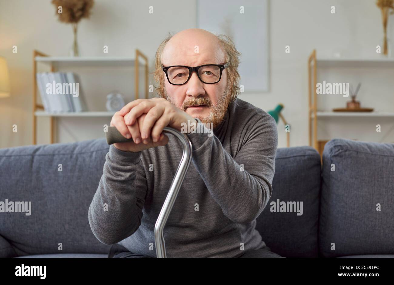 Porträt eines älteren Mannes mit Stock, der zu Hause auf der Couch sitzt und in die Kamera schaut Stockfoto