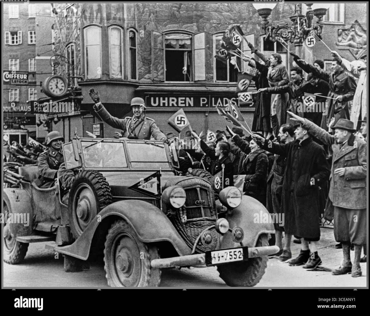 ANSCHLUSS ÖSTERREICH SALZBURG Österreichische Staatsbürger grüßen und schwenken fröhlich Hakenkreuzfahnen, während Soldaten der 2. SS-Panzerdivision „das Reich“ in einem Horch 830 R Kübelwagen durch Salzburg fahren. Die Veranstaltung fand kurz nach der Ankündigung des Anschlusses durch Adolf Hitler statt und markierte damit die Annexion Österreichs an Nazi-Deutschland am 12. März 1938. Stockfoto