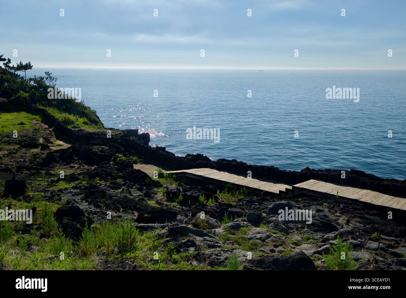 Kurze Holzstege durchqueren schwarze vulkanische Felsen über dem offenen Meer, eine ruhige Ecke des Handam Coastal Walk unter hellem Sonnenschein. Stockfoto