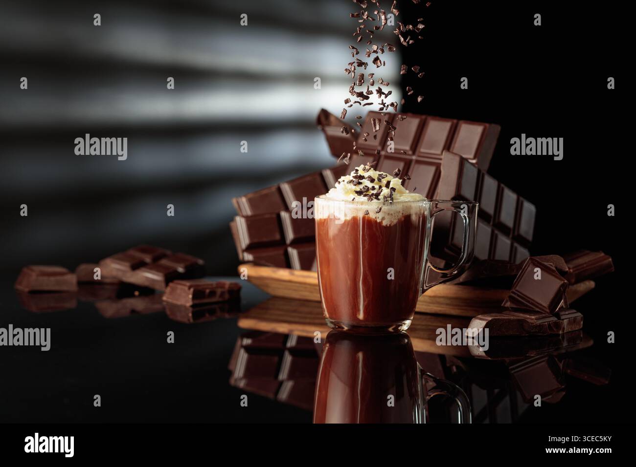 Heiße Schokolade mit Schlagsahne, bestreut mit Schokoladenbrösel. Auf einem Hintergrund zerbrochene Bitterschokoladentafeln. Schwarzer reflektierender Hintergrund. Stockfoto