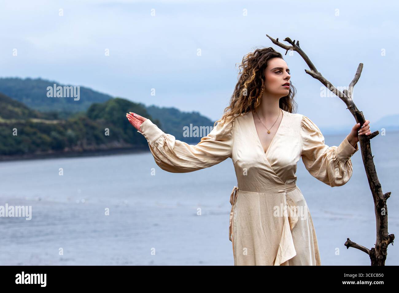 Fantasy-Shooting „Lady of the Lake“ am Wormit Beach, Fife, Schottland, während die Frau in Seidengewändern an den Felsen posiert, die Treibholz in der Hand halten Stockfoto