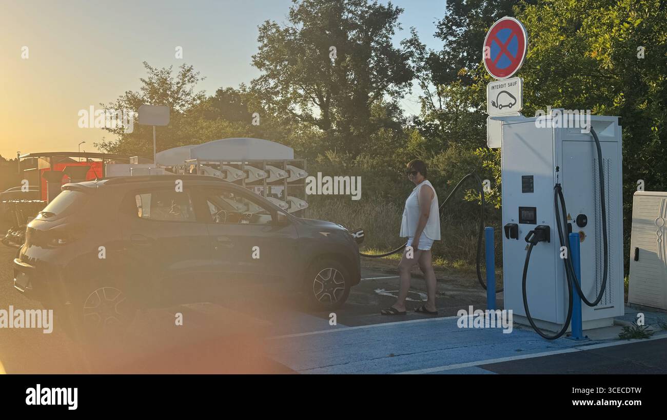 Die Frau schaltet die Autoladestation ein, während sie ihr Elektrofahrzeug auflädt. Konzept intelligenter Technologien für komfortables Wohnen, Elektrofahrzeuge Stockfoto