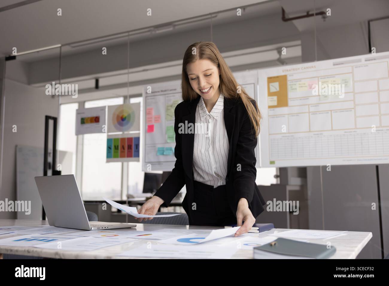 Positiv zufriedene junge Berufsfrau, die Marketingdaten überprüft Stockfoto