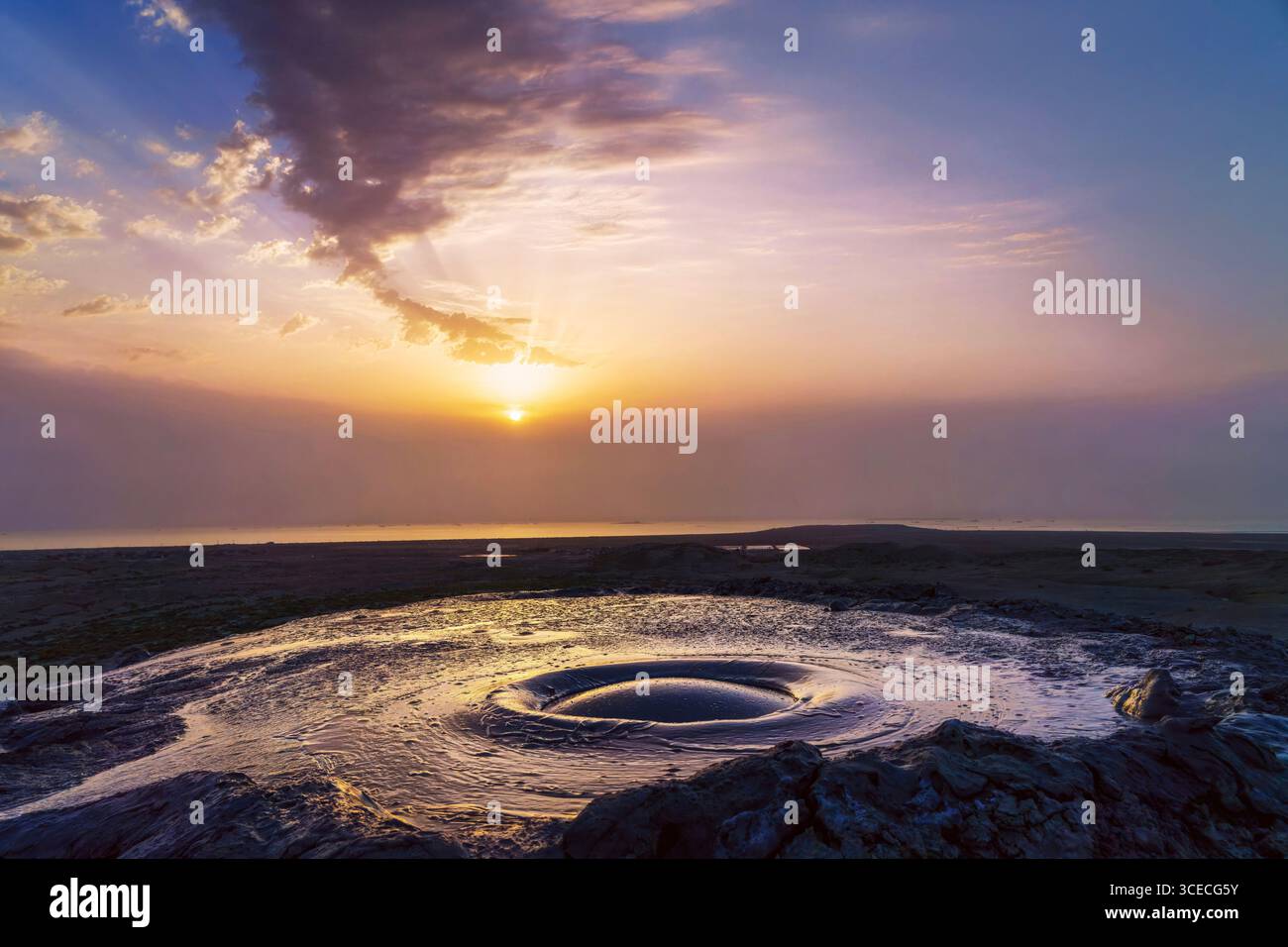Aktiver Schlammvulkan sprudelt beim Sonnenaufgang mit dem Kaspischen Meer im Hintergrund in Gobustan, Aserbaidschan Stockfoto