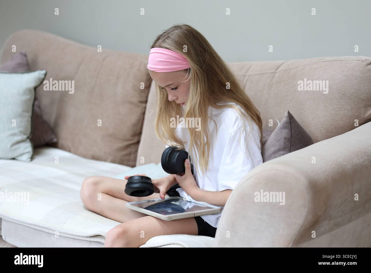 Mädchen sitzt auf dem Sofa mit Tablet-Technologie und hält Kopfhörer Touchscreen mit Daumenkonzept Bildschirmzeit Bildschirmzeit Stockfoto