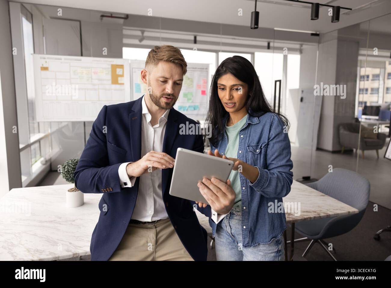 Junger kaukasischer Geschäftsmann, der einer indischen Kollegin Tablette zeigt Stockfoto