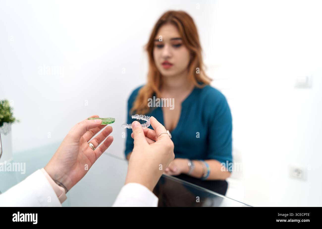 Ein Zahnarzt stellt einem Patienten in einer modernen Klinik Zahnausleger vor. Die Patientin, eine junge Frau, hört aufmerksam zu und hebt einen Profi hervor Stockfoto