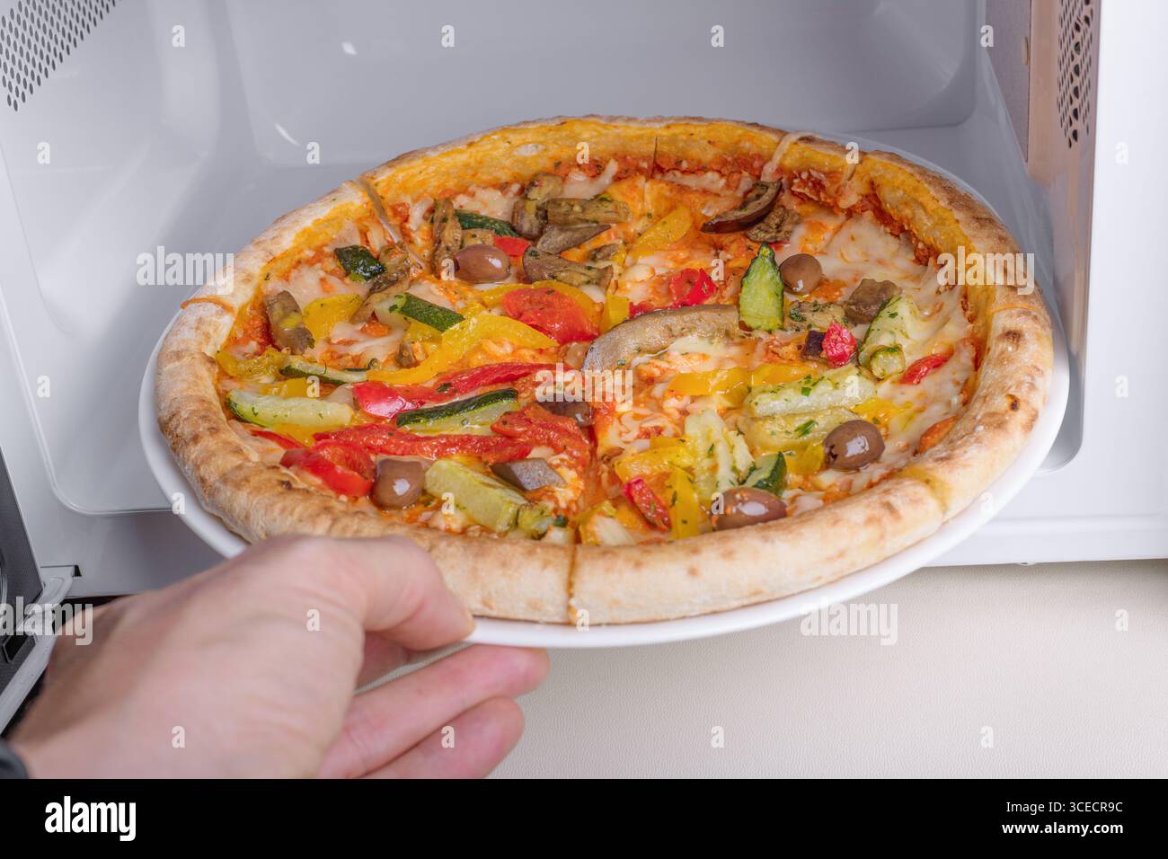 Eine frische vegetarische Pizza mit bunten Paprika, Oliven und Zucchini wird aus der Mikrowelle genommen und bietet eine köstliche und gesunde Mahlzeit Stockfoto