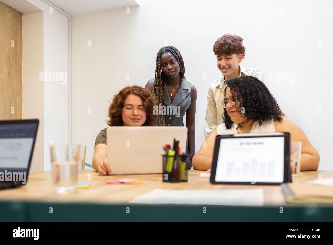 Eine vielfältige Gruppe junger Kollegen arbeitet in einem modernen Büroumfeld um einen Laptop herum. Die Umgebung ist inklusiv und professionell, mit t Stockfoto