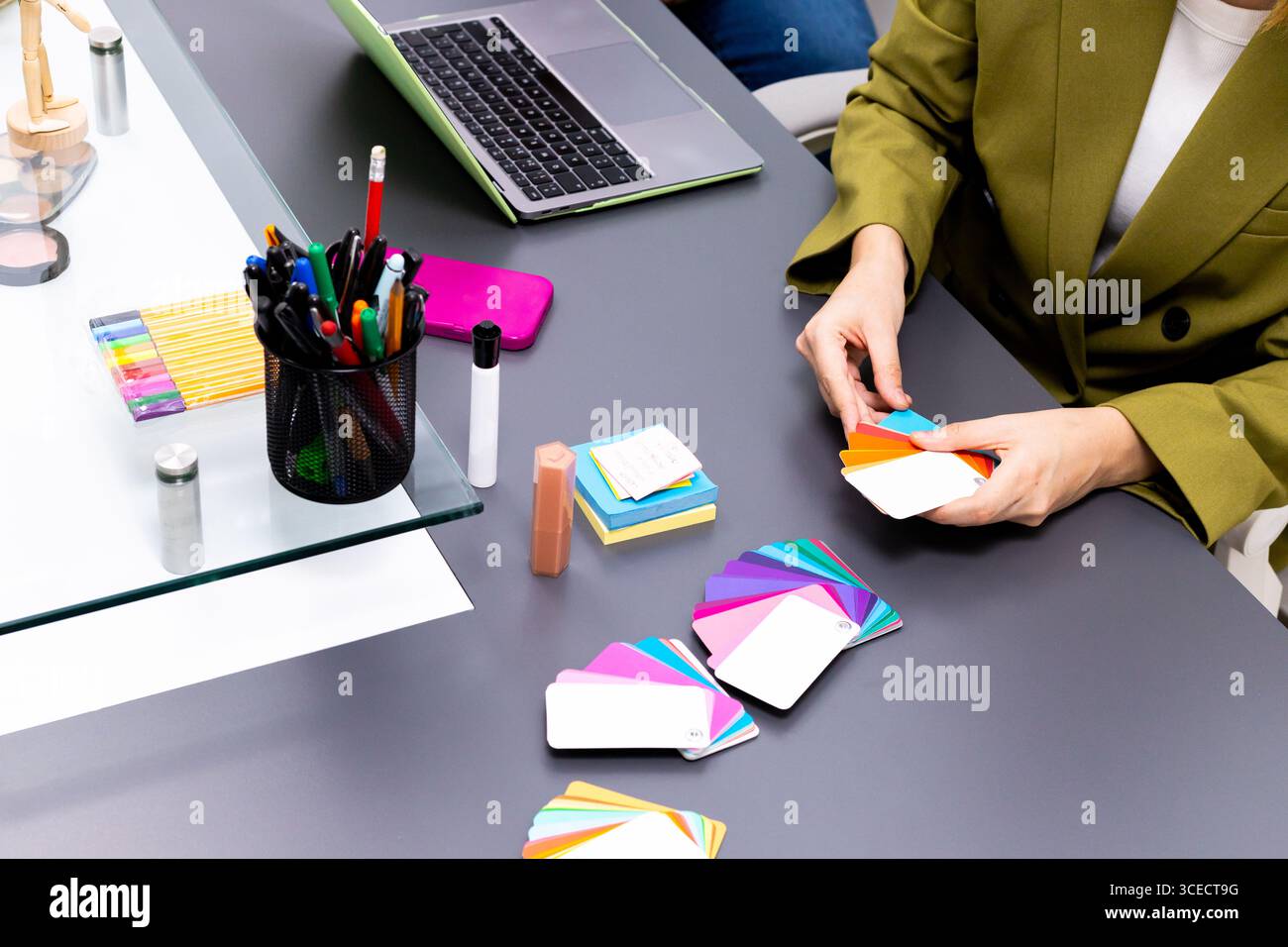 Ein professioneller Bildberater arrangiert eine Reihe von farbenfrohen Farbfeldern auf einem Tisch. Werkzeuge wie Schreibwaren und ein Laptop sind sichtbar und heben ein Werk hervor Stockfoto