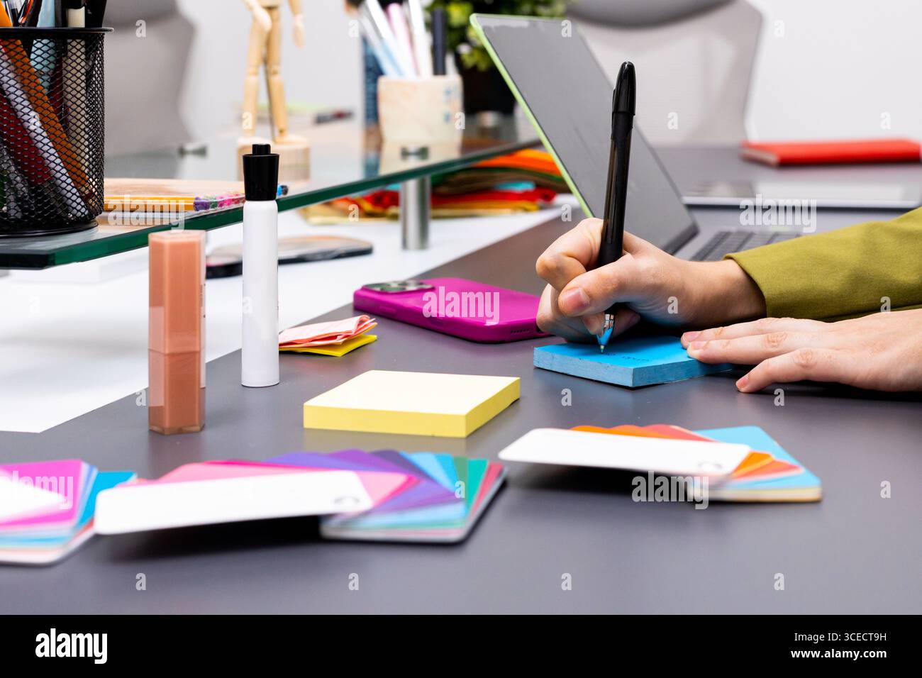 Ein kreativer Arbeitsbereich mit Handschrift auf einem blauen Notizblock, umgeben von farbenfrohen Werkzeugen, die eine dynamische Bildberatungsumgebung darstellen Stockfoto