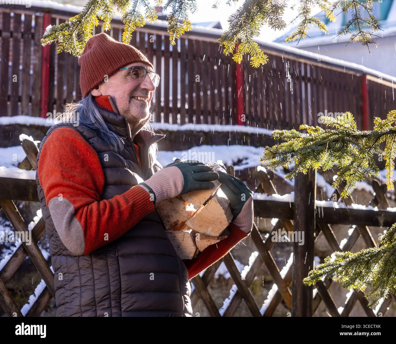 Ein älterer Mann trägt Winterkleidung und hält draußen Ökofeuerholz. Er scheint glücklich und entspannt zu sein und hebt einen nachhaltigen Lebensstil in einer Kuppel hervor Stockfoto