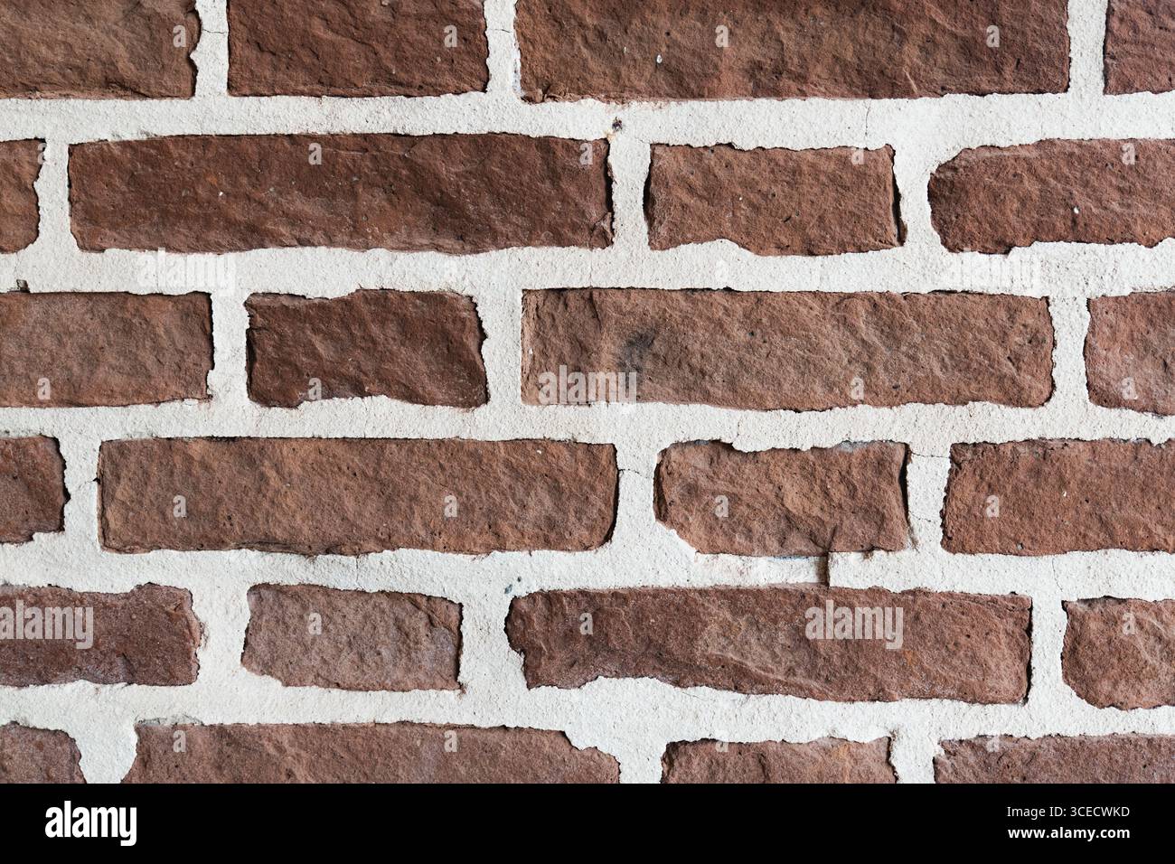 Nahaufnahme einer roten Ziegelwand mit einer robusten, strukturierten Oberfläche mit hellweißen Mörtelfugen. Die Rauheit und Farbe der Steine sorgen für einen Schlag Stockfoto
