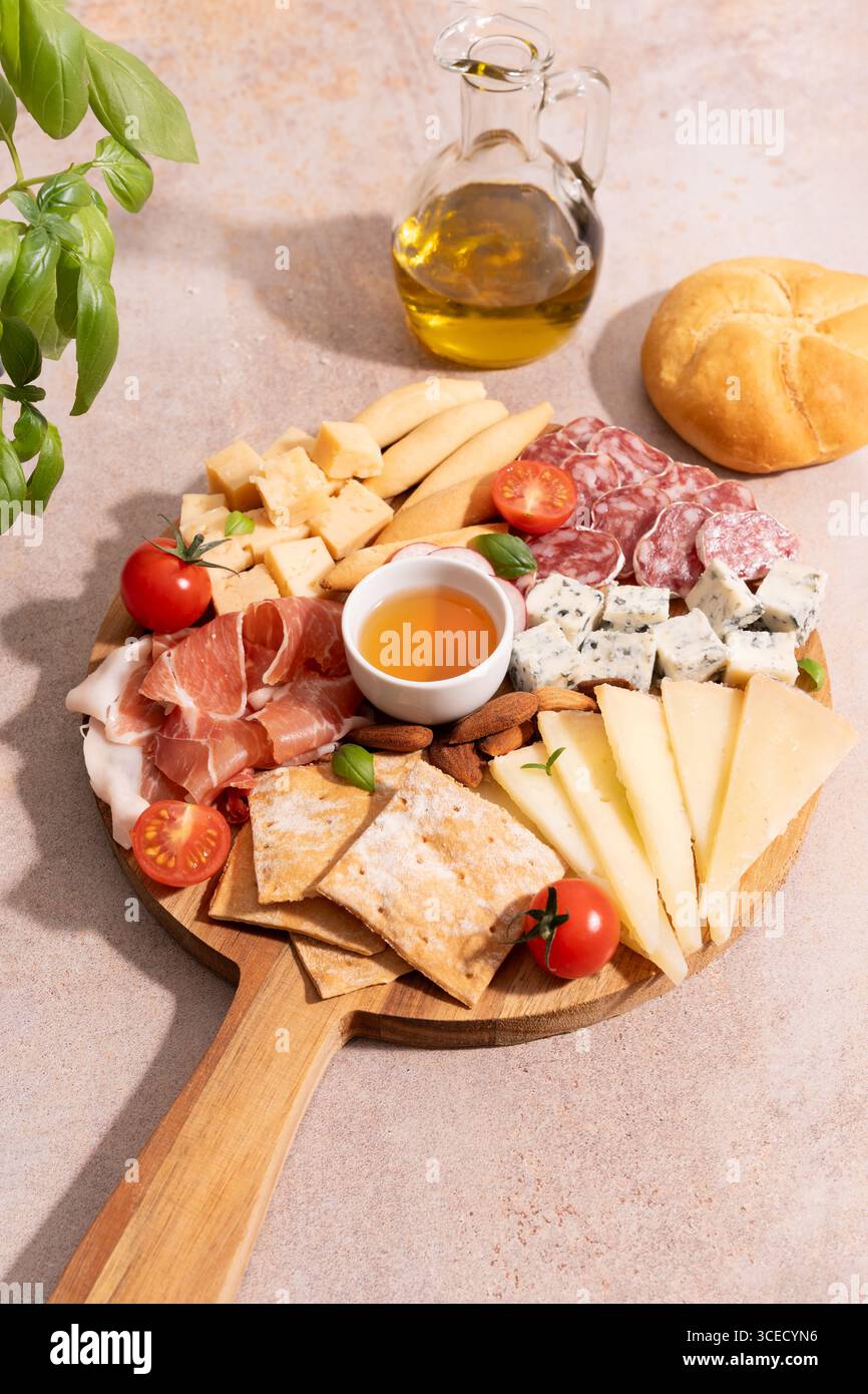 Blick von oben auf eine Holzplatte mit verschiedenen Käsesorten, Wurstwaren, Kirschtomaten, Crackern und Mandeln. Eine kleine Schüssel Honig ergänzt das AR Stockfoto