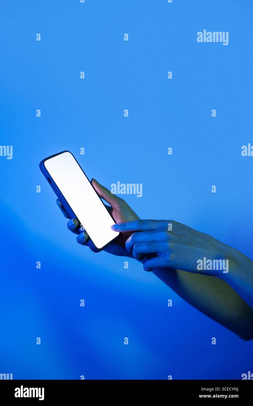 Eine Hand interagiert mit einem modernen Smartphone und leuchtet unter leuchtenden Neonlichtern. Das farbenfrohe Ambiente unterstreicht Technologie und Konnektivität in einer Digitalkamera Stockfoto