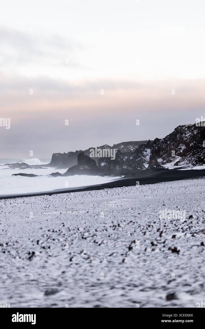 Die abgelegene isländische Küste wird im Winter mit dramatischen schwarzen Sandstränden, die mit Schnee bedeckt sind, und zerklüfteten Klippen unter weichem Pastellfarben erfasst Stockfoto