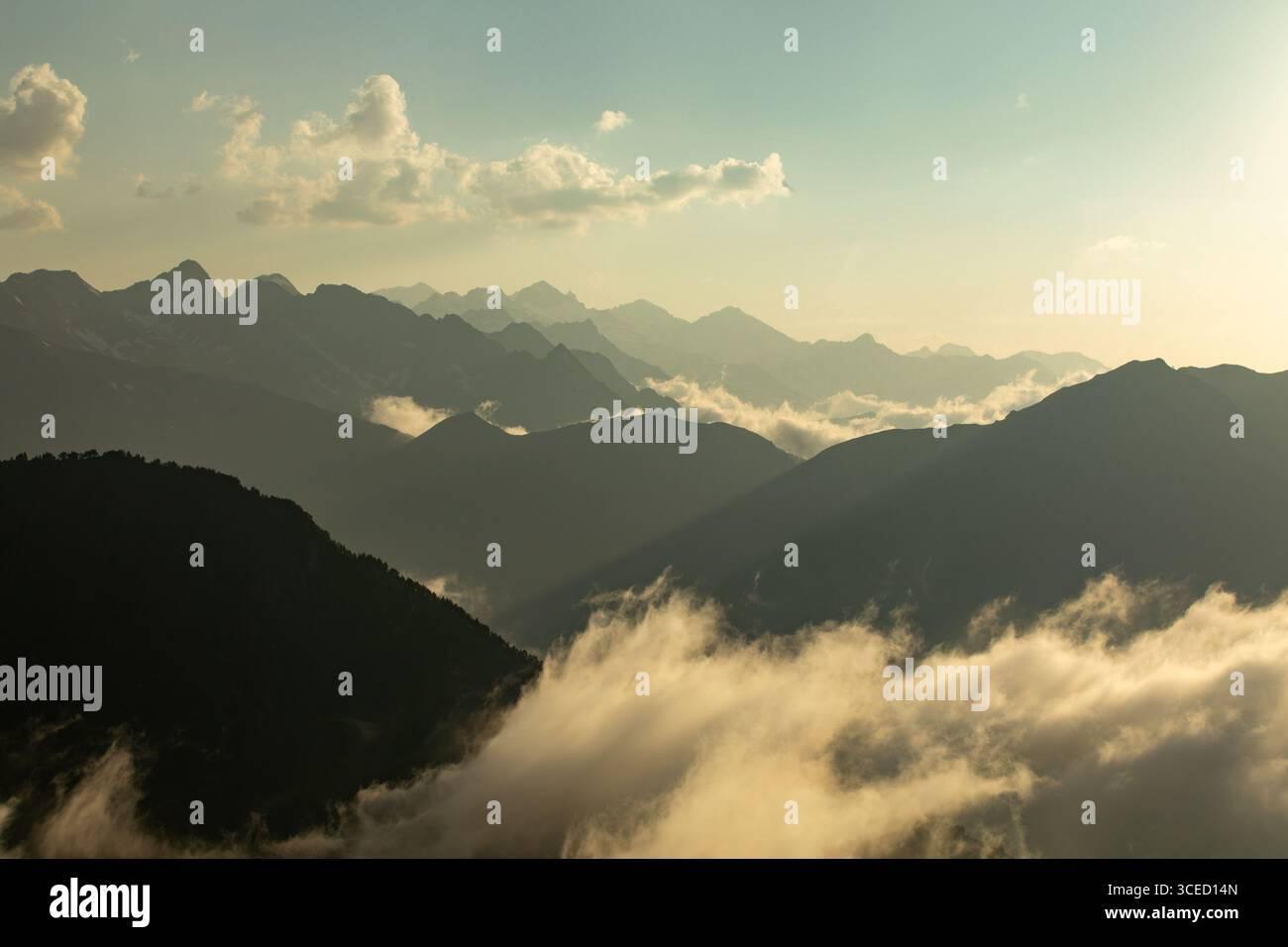 Ein atemberaubender Blick auf nebelbedeckte Berge unter einem goldenen Sonnenaufgang. Wolken treiben zwischen den Gipfeln und schaffen eine ruhige und ätherische Atmosphäre im Ohr Stockfoto