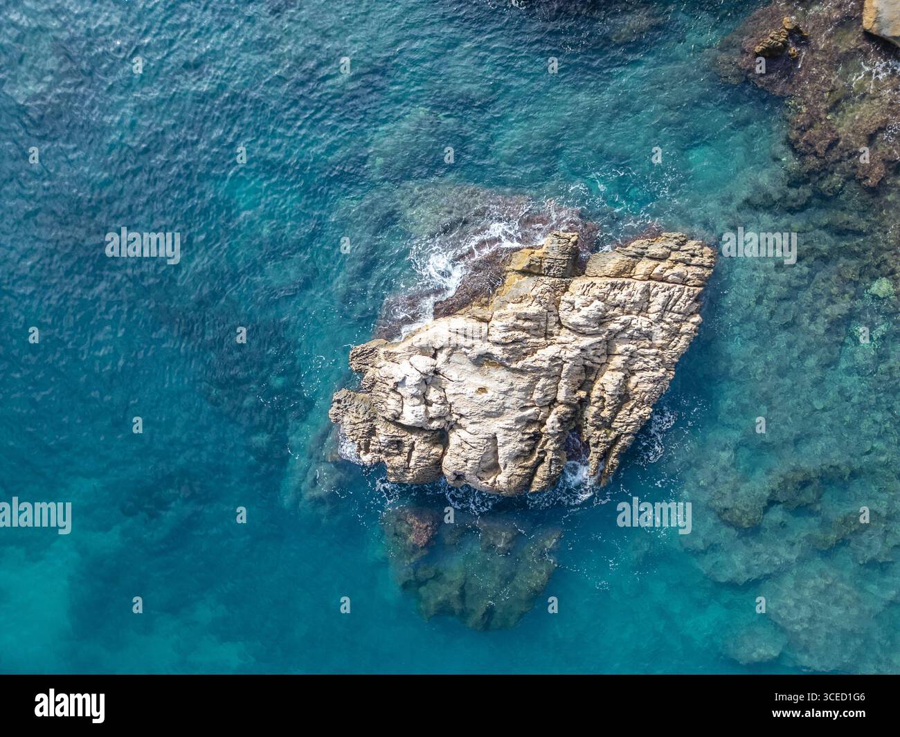 Ein Blick aus der Vogelperspektive fängt einen zerklüfteten Felsvorsprung ein, umgeben von klarem azurblauem Wasser des Mittelmeers, und zeigt die natürliche Schönheit der Costa Blanc Stockfoto