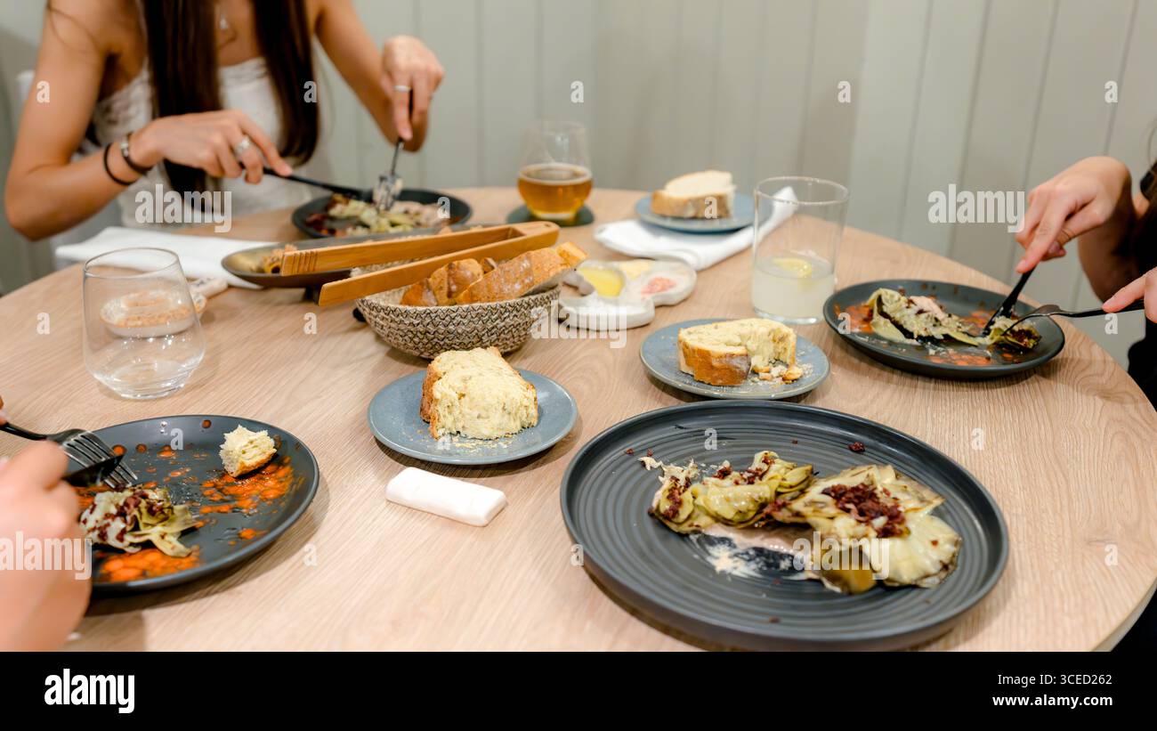 Eine gemütliche Speiseszene mit Freunden, die eine Mahlzeit teilen. Der Tisch bietet eine Vielzahl köstlicher Gerichte, Brot und Getränke, die die Essenz eines warmen Moments einfangen Stockfoto