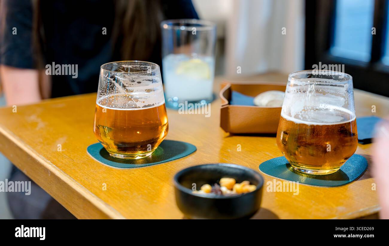 Ein gemütlicher Restauranttisch mit zwei Bieren und einem Zitronengetränk, begleitet von einem Gericht mit gemischten Nüssen, die eine entspannte Atmosphäre für einen Abend schaffen Stockfoto