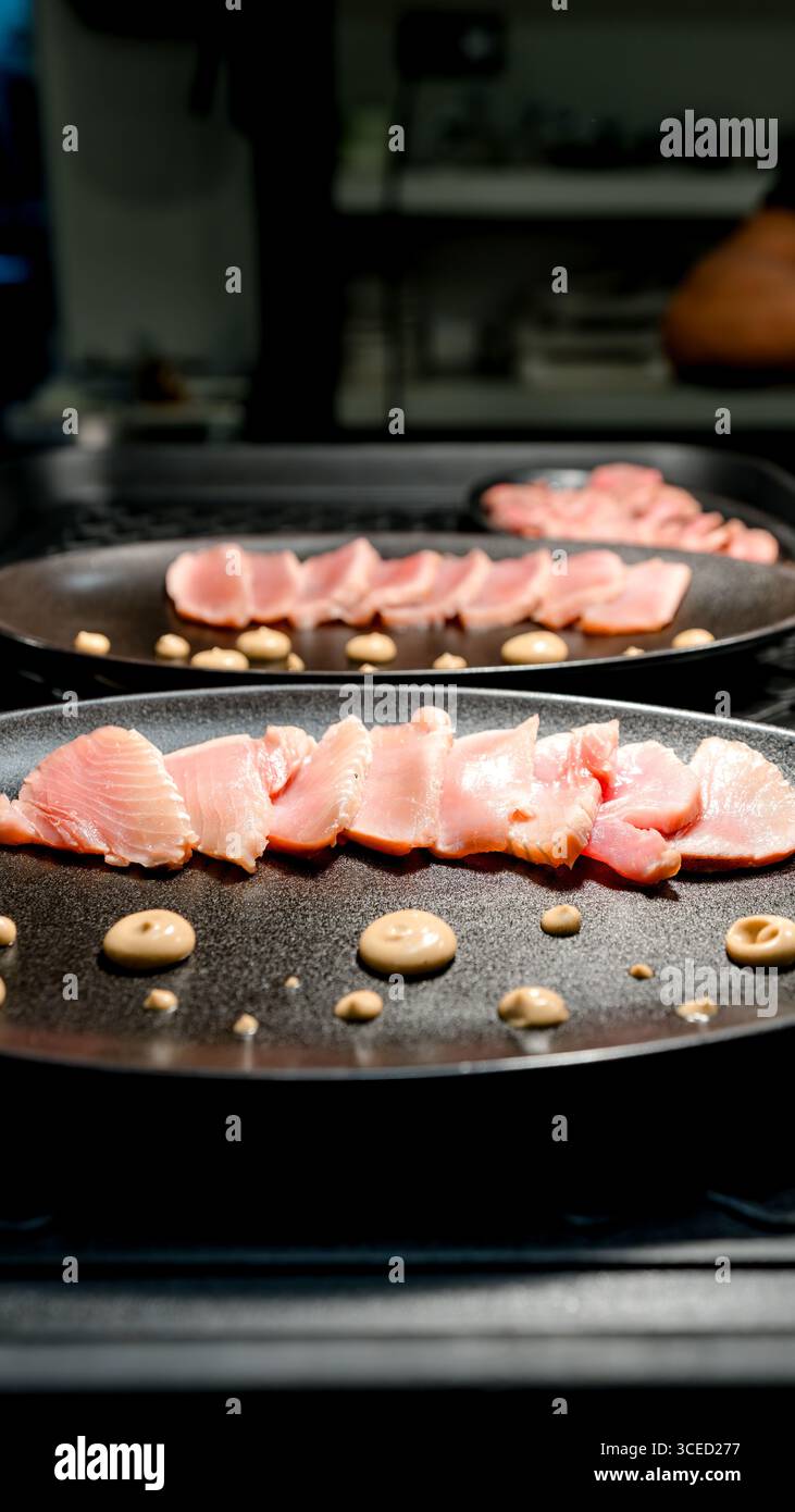 Dünn geschnittene Meeresfrüchte, kunstvoll auf einem schwarzen Teller mit dekorativen Soßenpunkten angeordnet, perfekt für ein Gourmet-Dining-Erlebnis in einem eleganten Restaurant Stockfoto