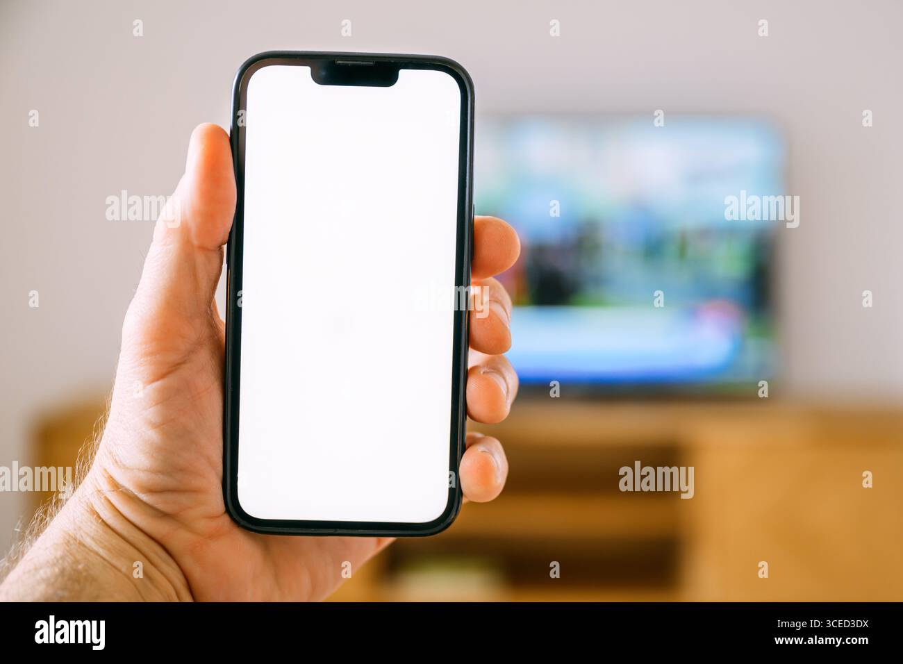 Smartphone-Mockup-Bildschirm, Mann hält Handy vor Smart TV-Gerät, tv Remote App und tv-Programm-Auflistung Konzept, selektiver Fokus Stockfoto