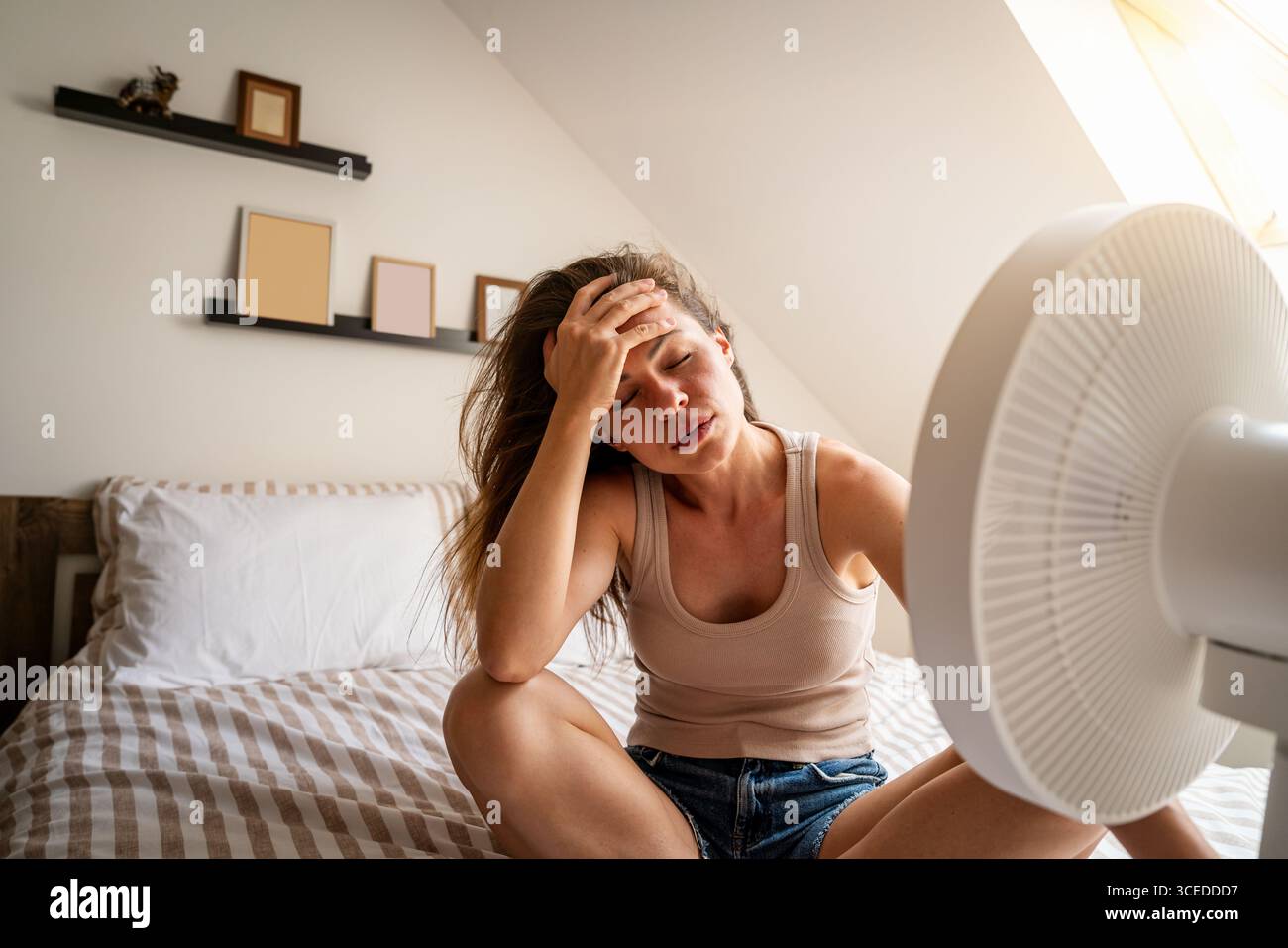 Überhitzte Frau, die zu Hause mit Ventilator abkühlen will Stockfoto